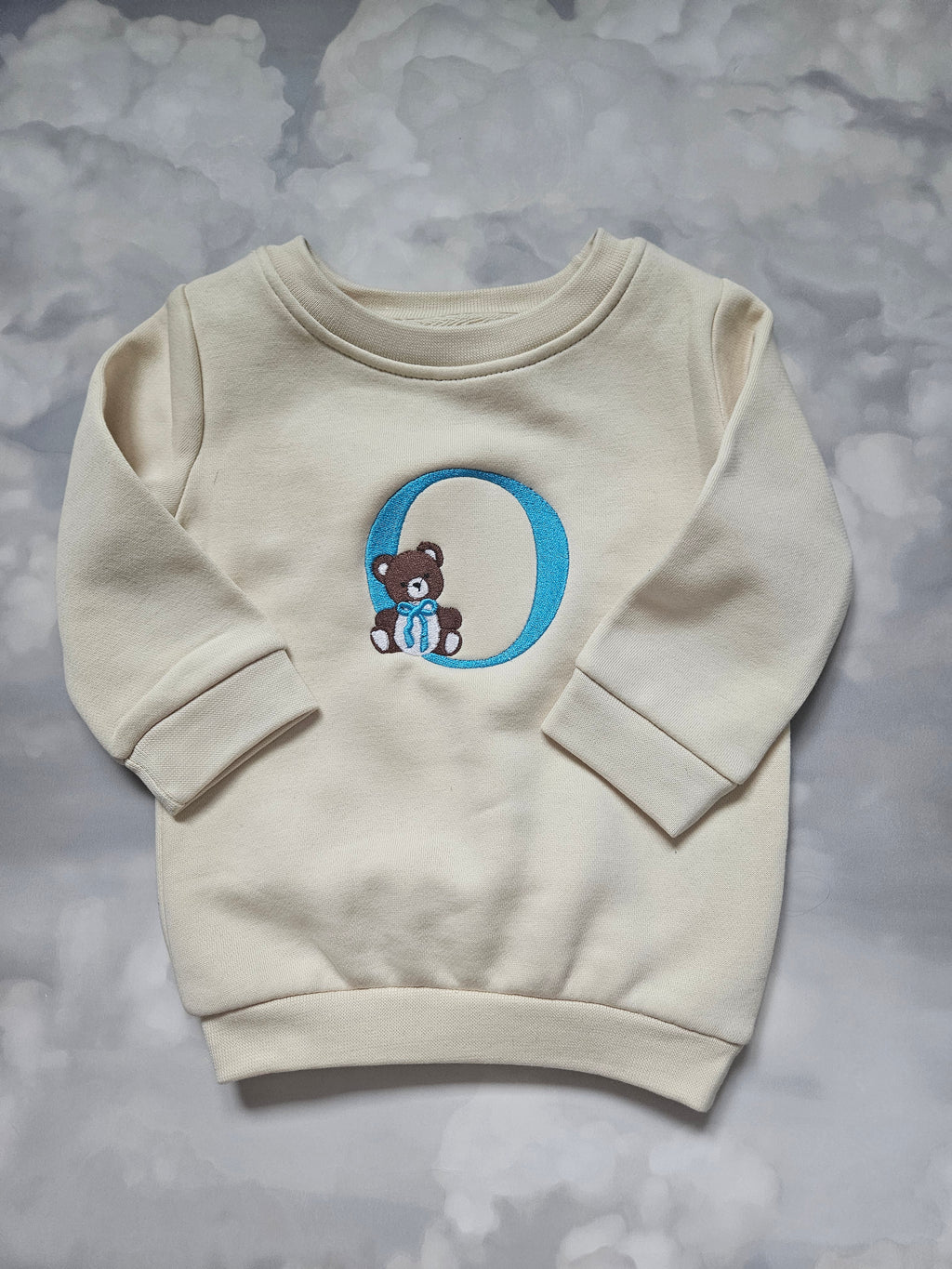 Beige hoodie with a blue and white logo on a gray background