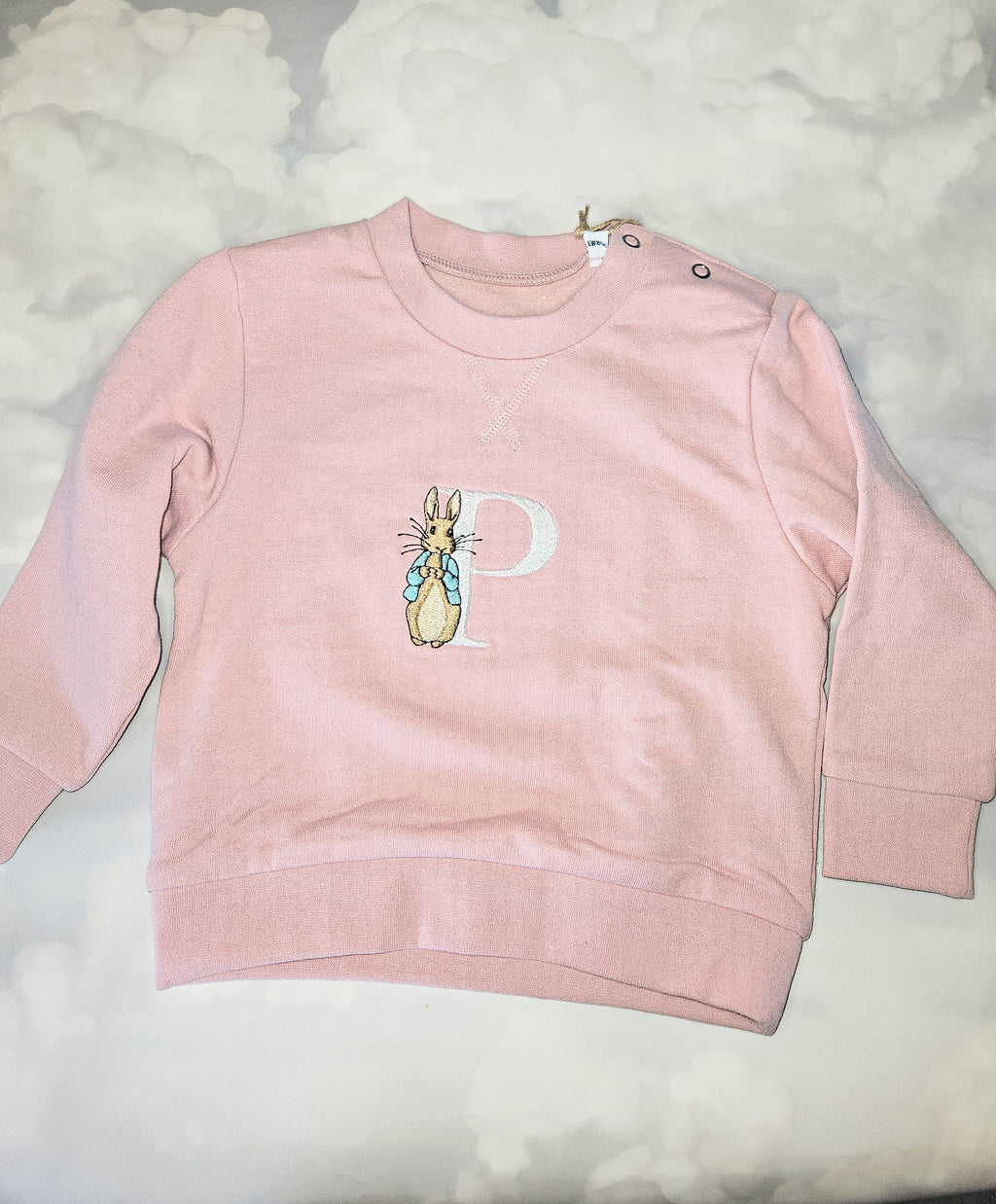 Pink sweatshirt with a cartoon character and letter 'P' on a light gray background