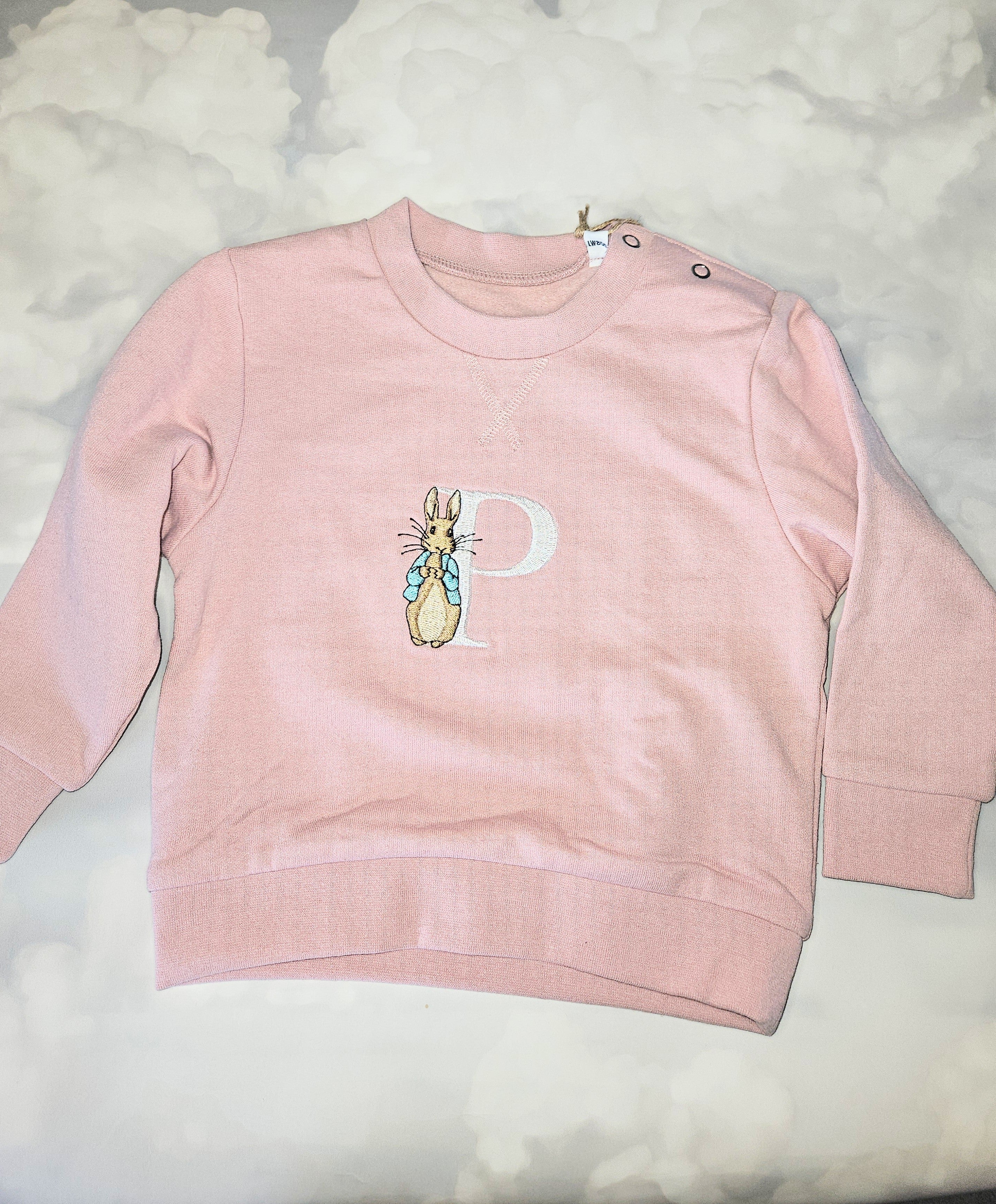 Pink sweatshirt with a cartoon character and letter 'P' on a light gray background