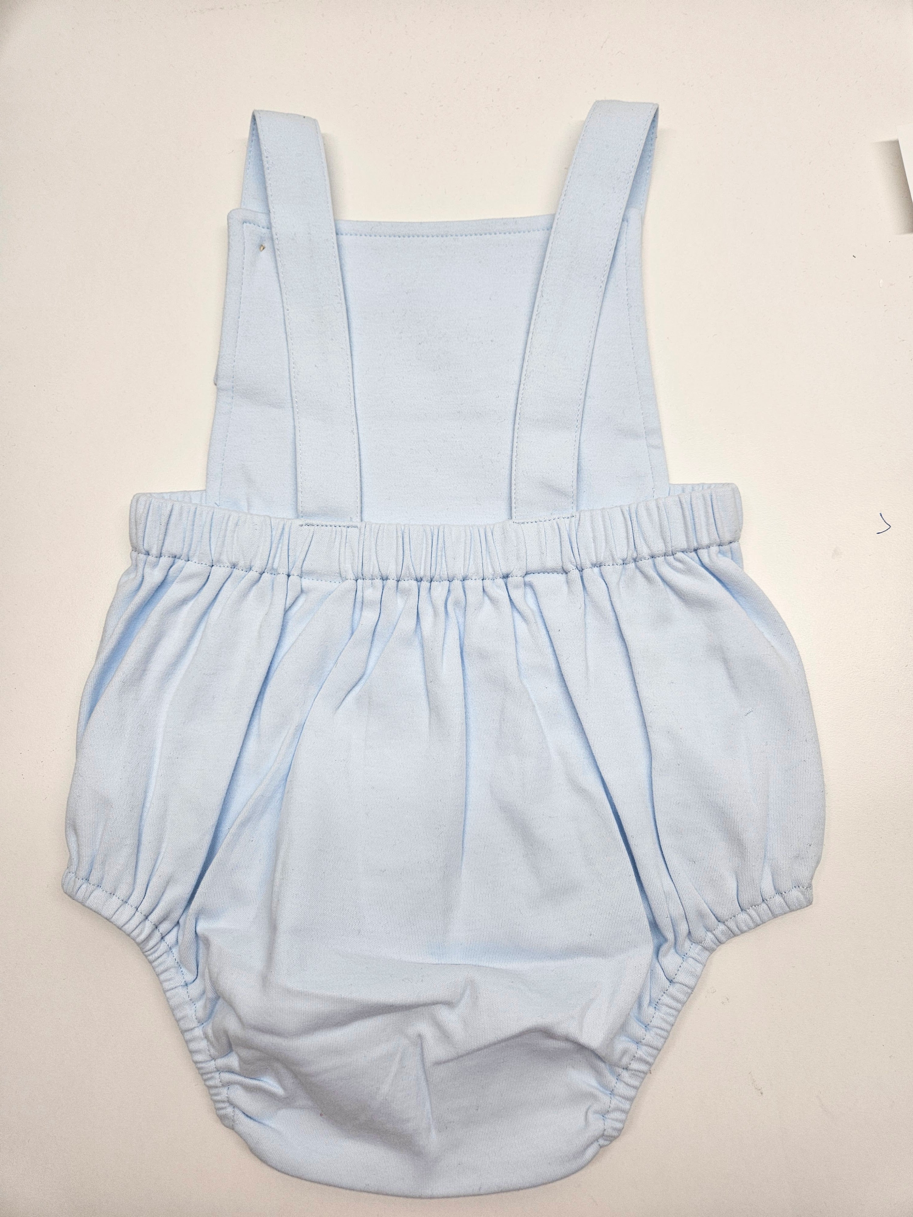 A light blue baby romper with wide shoulder straps and a gathered elastic waist, laid flat on a light beige background.